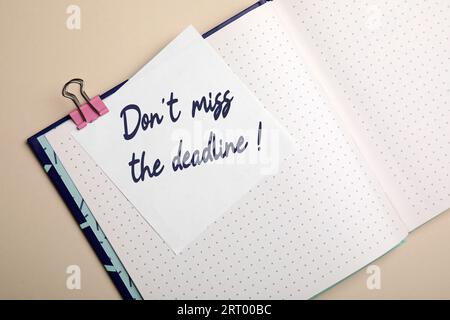 Nota con promemoria non perdere la scadenza nel notebook su sfondo beige, vista dall'alto Foto Stock