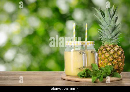 Gustoso frullato di ananas in vasetti mason su un tavolo in legno su sfondo sfocato, spazio per il testo Foto Stock