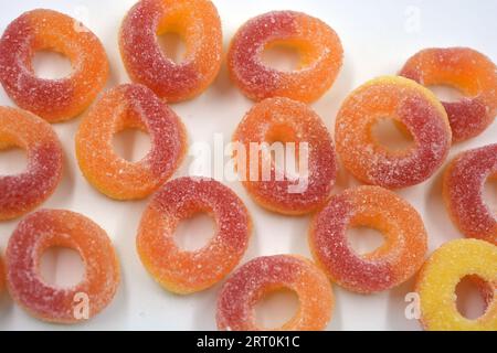 Dolci bellissimi e colorati sotto forma di ciambelle rosse e arancio in polvere di zucchero, disposti su uno sfondo bianco opaco. Foto Stock