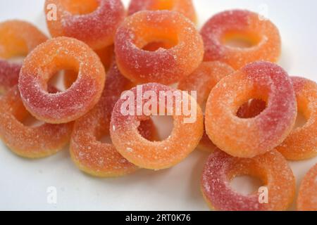 Dolci bellissimi e colorati sotto forma di ciambelle rosse e arancio in polvere di zucchero, disposti su uno sfondo bianco opaco. Foto Stock