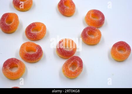 Dolci bellissimi e colorati sotto forma di ciambelle rosse e arancio in polvere di zucchero, disposti su uno sfondo bianco opaco. Foto Stock