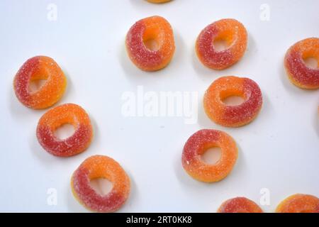 Dolci bellissimi e colorati sotto forma di ciambelle rosse e arancio in polvere di zucchero, disposti su uno sfondo bianco opaco. Foto Stock