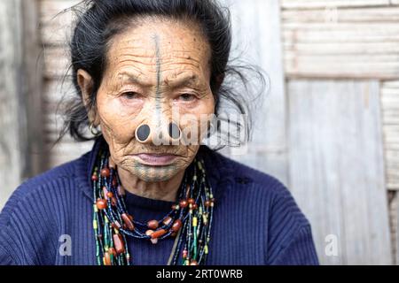 Donna della tribù degli apatani in una casa di un piccolo villaggio vicino a Ziro, con tradizionali tatuaggi facciali e tappi per naso tradizionali, Ziro, India Foto Stock