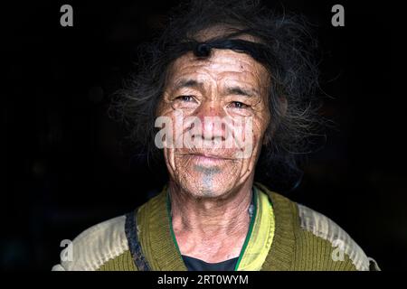 Un uomo anziano della tribù Apatani che indossa abiti tessuti tradizionali e un cappello distintivo, all'interno di un villaggio rurale della valle di Ziro, in India. Foto Stock