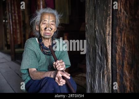 Donna della tribù degli apatani in una casa di un piccolo villaggio vicino a Ziro, con tradizionali tatuaggi facciali e tappi per naso tradizionali, Ziro, India Foto Stock