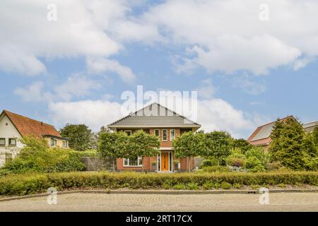 una casa nel mezzo di una zona urbana con alberi e cespugli che crescono su entrambi i lati della strada, Foto Stock