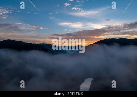 Una vista panoramica di una lussureggiante valle verde avvolta da una fitta nebbia, con un sereno cielo blu sullo sfondo Foto Stock