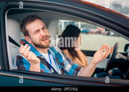 Istruttore in malinteso, seduto sul sedile del passeggero in un'auto accanto a una donna che non ha superato il test di guida. Test di guida, corsi per conducenti, esame Foto Stock