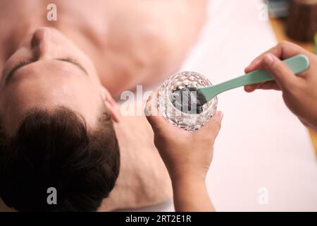 Estetista che applica la maschera di carbone sul viso del cliente maschile Foto Stock