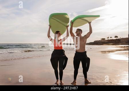 Coppia felice che si diverte sulla spiaggia, tenendo le tavole da surf sopra la testa Foto Stock