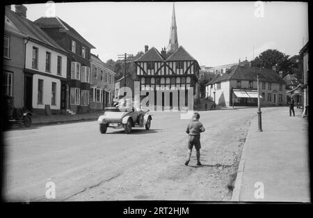 Town Street, Thaxted, Uttlesford, Essex, c1920. Una vista che guarda a nord-ovest lungo Town Street a Thaxted verso la Guildhall, con un'auto che passa davanti a un giovane ragazzo in primo piano. Foto Stock