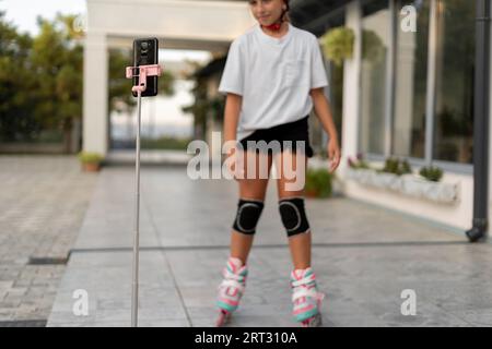 Bambina che cavalca sui pattini a rotelle all'aperto, bambina che gioca sui pattini a rotelle e registra video per il suo blog. Foto Stock