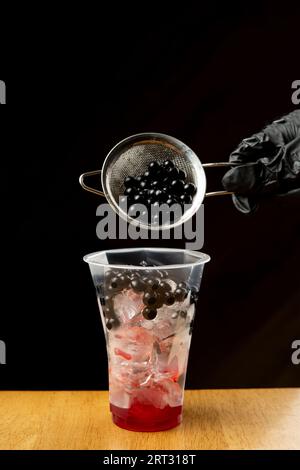 Versare mini perle di boba marrone in un bicchiere di plastica di tè al latte freddo Foto Stock