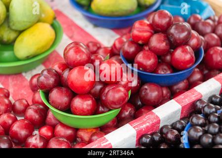 Tavolo con cesto di prugne e manghi accatastati al mercato di strada Foto Stock