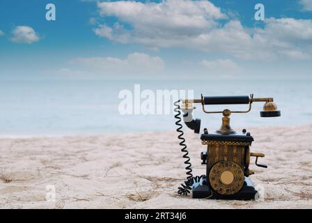 Un vecchio telefono steso sulla sabbia sullo sfondo del mare. Foto Stock