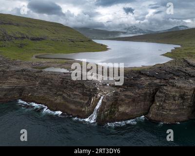 Cascata e scogliere di Traelanipa con il lago sopra l'oceano, Isole Faroe, Danimarca, Europa, vista aerea Foto Stock
