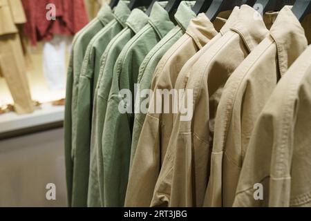 Le camicie a maniche lunghe verdi e marroni sono appese alle grucce di un negozio di abbigliamento. Primo piano. Foto Stock