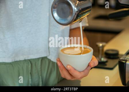 Una giovane barista che prepara un delizioso cappuccino Foto Stock