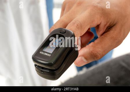 Dito di un adulto asiatico dall'India utilizzando un pulsossimetro nello studio medico. Foto Stock