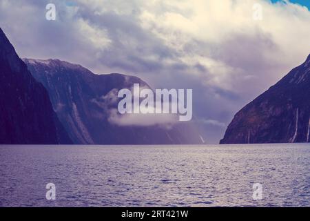 Foto di montagne tra nuvole e nebbia viste dall'acqua nel Milford Sound nel Fiordland National Park sull'Isola del Sud della nuova Zelanda Foto Stock