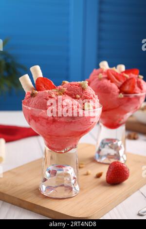 Deliziose palline di gelato alla fragola con bastoncini di cialda e noci in ciotole da dessert in vetro servite su un tavolo bianco Foto Stock