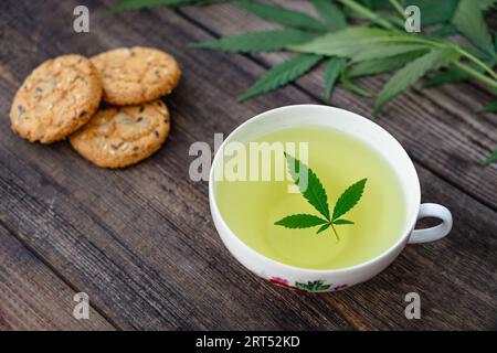 Tè di cannabis erbe su tazza di tè e biscotti con semi con foglie di cannabis foglie di marijuana erbe, tè salutare con foglie di canapa THC CBD erbe alimentari e. Foto Stock