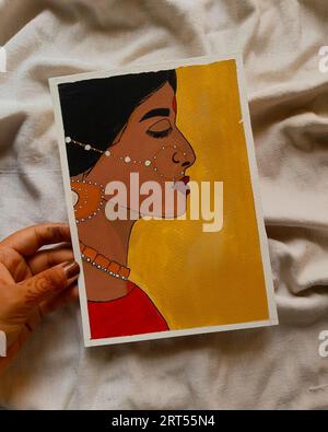 Un primo piano di una mano che regge un colorato dipinto acrilico di una donna con orecchini d'oro Foto Stock