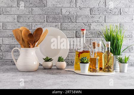 Bottiglie di vetro con vari tipi di olio sul ripiano della cucina all'interno di una cucina moderna con piante verdi da interno. Muro di mattoni grigi Foto Stock