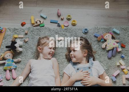 Vista dall'alto dei bambini che giocano con giocattoli colorati. Ritratto di bambini sdraiati sul tappeto nella camera da letto o nell'asilo. Due sorelle sorridenti felici. Giochi educativi ecologici Foto Stock