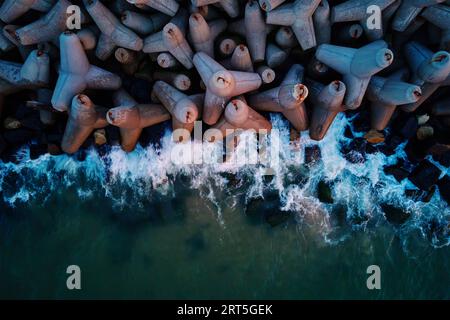 Le onde si infrangono sulle frangiflutti in cemento tetrapod sulla costa del mare. Protezione da onde grandi. Costa del Mar Baltico al porto di Wladyslavovo al tramonto Foto Stock