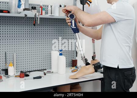 Ritagliare un artigiano irriconoscibile che regola e piega la gamba protesica moderna nella sezione del ginocchio Foto Stock