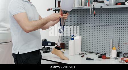 Ritagliare un artigiano irriconoscibile che regola e piega la gamba protesica moderna nella sezione del ginocchio Foto Stock