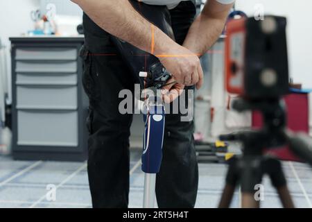 Ritagliare un artigiano irriconoscibile che regola e piega la gamba protesica moderna nella sezione del ginocchio Foto Stock