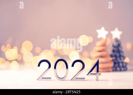 Numeri di metallo 2024 su un tavolo bianco con alberi di Natale e luci bokeh. L'idea di felice anno nuovo 2024 sta per arrivare. Foto Stock