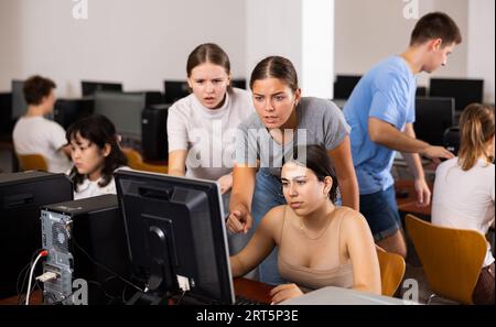 Insegnante che spiega la soluzione del compito a giovani ragazze e ragazzi durante la lezione di informatica Foto Stock