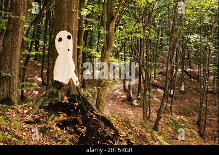 Silhuette bianca dell'uomo o aliena raffigurata su un albero della foresta, ricoperta di foglie gialle secche, con un'altra di queste silhuette sullo sfondo. Paesaggistico, bellissimo Foto Stock