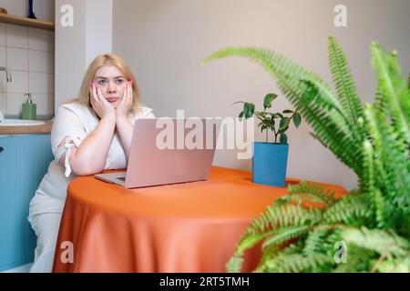 Donna stanca e sovraccarica di lavoro seduta in stress o in depressione a un tavolo con un notebook. Persona annoiata da sola. Foto Stock