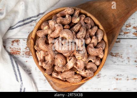 Anacardi con guscio in un recipiente di legno. Anacardi sgusciati su sfondo di legno bianco. Vista dall'alto Foto Stock