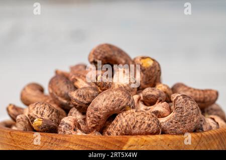 Anacardi con guscio in un recipiente di legno. Anacardi sgusciati su sfondo di legno bianco. Primo piano Foto Stock