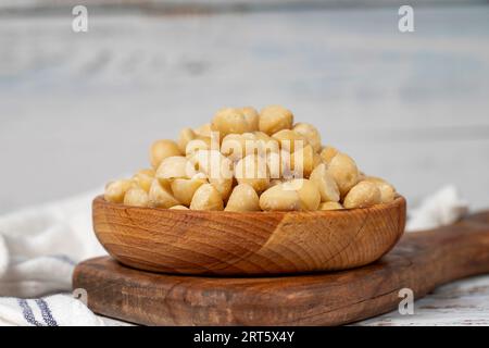 Noce di macadamia in un recipiente di legno. Noci di macadamia sbucciate su fondo di legno bianco Foto Stock