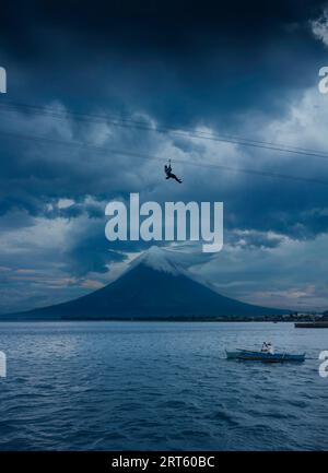 Uomo in zipline sopra la baia di Legazpi City con il vulcano Mayon. Foto Stock