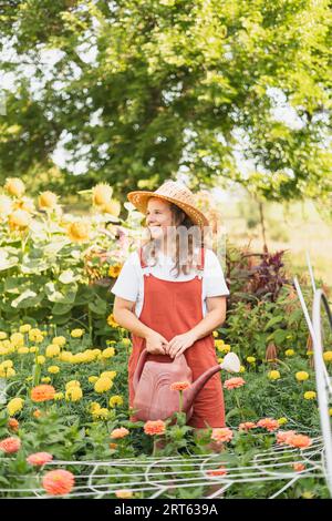 Una donna sorridente che annaffiava i suoi fiori rosa e giallo con un rosso Foto Stock