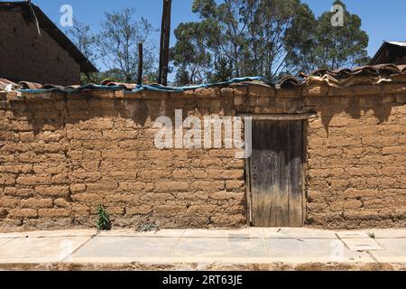Vecchia porta in legno sulla facciata in mattoni di adobe alla luce del sole nelle ande Foto Stock