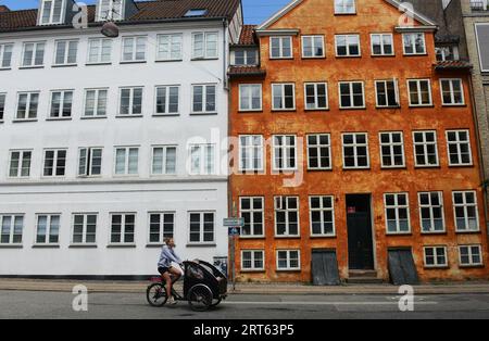 Una donna danese che pedala di fronte a un edificio colorato lungo Åbenrå nel centro di Copenaghen, Danimarca. Foto Stock