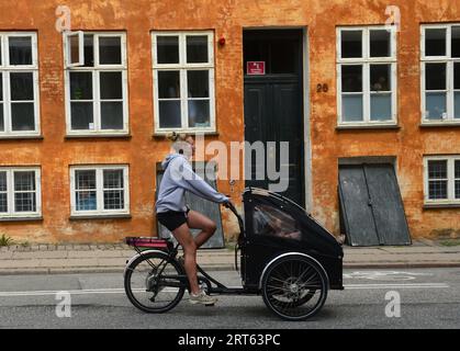 Una donna danese che pedala di fronte a un edificio colorato lungo Åbenrå nel centro di Copenaghen, Danimarca. Foto Stock