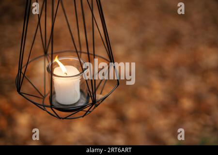 Moderna lanterna nera minimalista con candela a fuoco sullo sfondo delle foglie autunnali nella foresta. Ciao, autunno! Lanterna luminosa in morbidi boschi autunnali. Copia Foto Stock