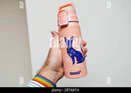 Parigi, Francia - 3 giu 2023: Una mano maschile afferra con sicurezza una lattina SIGG color rosa per i viaggi in acqua, evidenziandone la tonalità e il design vivaci Foto Stock