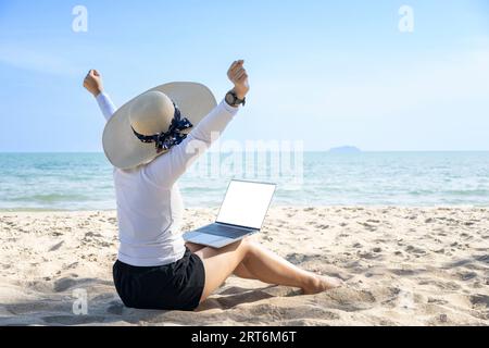 Concetto di lavoro da qualsiasi luogo. Vista posteriore della giovane donna che lavora su un computer portatile sulla spiaggia Foto Stock