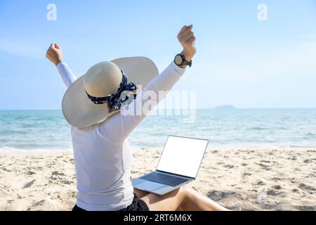 Concetto di lavoro da qualsiasi luogo. Vista posteriore della giovane donna che lavora su un computer portatile sulla spiaggia Foto Stock