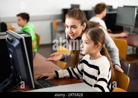 L'insegnante insieme agli studenti conduce una lezione sull'educazione informatica Foto Stock